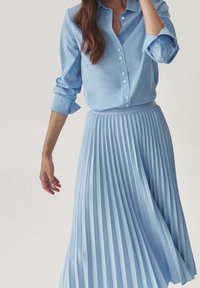 Gonna plissettata azzurro chiaro abbinata a una camicia con bottoni coordinata, caratterizzata da una texture liscia e un design colletto classico, offrendo un look coordinato.