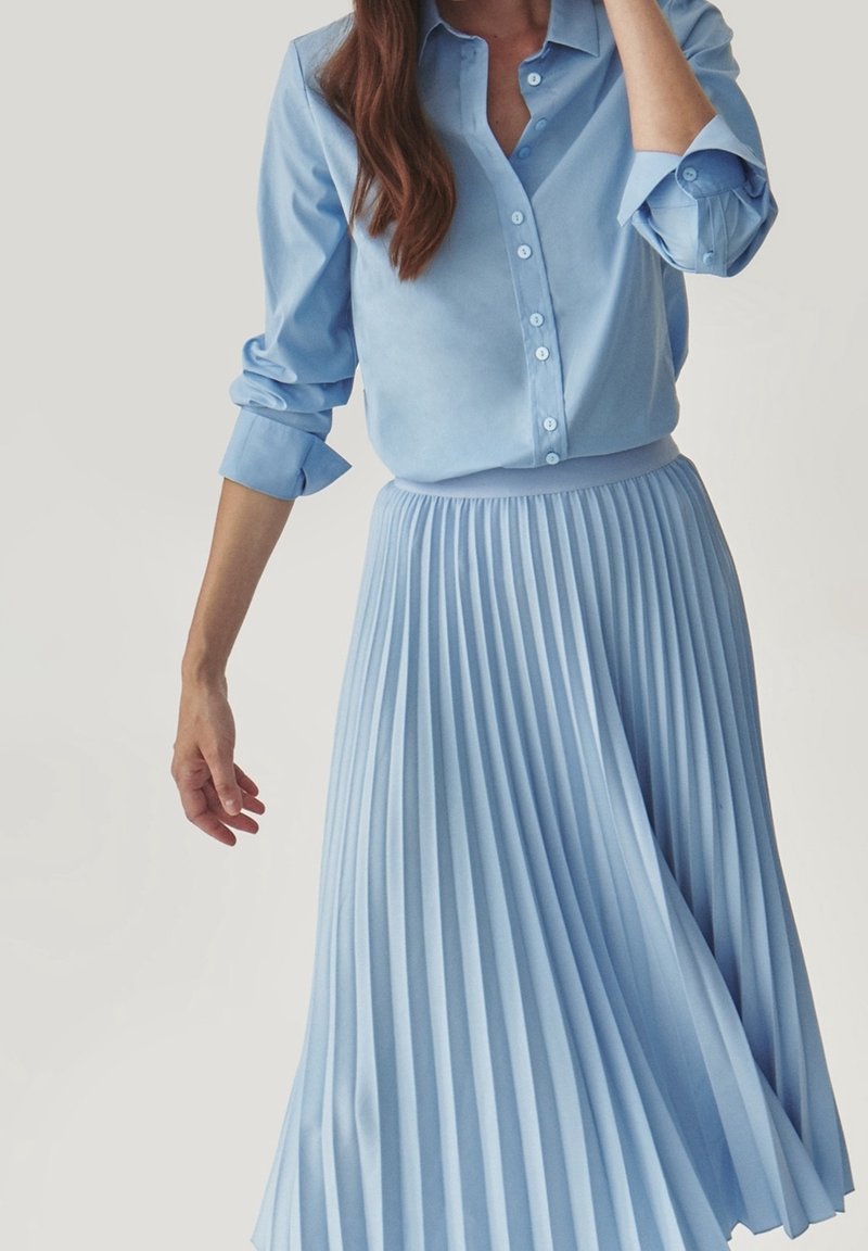 Gonna plissettata azzurro chiaro abbinata a una camicia con bottoni coordinata, caratterizzata da una texture liscia e un design colletto classico, offrendo un look coordinato.