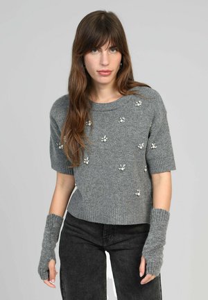 Un pull gris à manches courtes avec des embellissements floraux, un col et un ourlet côtelés, porté avec des gants gris sans doigts, sur un fond uni.