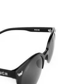 Černé sluneční brýle s lesklým povrchem, ve tvaru kočičích očí. Ramena zdobí tři stříbrné tečky a detail srdce poblíž pantů.