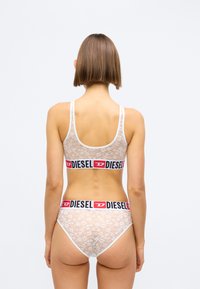 Hvit blonde bralette og matchende truse med en svart og rød Diesel logo-bånd. Stoffet har blomster mønstre og en myk tekstur.