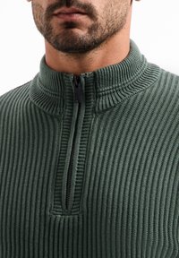 Groene geribbelde pullover met hoge hals, voorzien van een korte rits aan de voorkant en een textuurfinish.