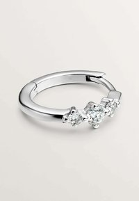Anillo de metal tono plateado que presenta tres piedras preciosas redondas y transparentes, engastadas en garras similares a garras, con una banda suave y curva.