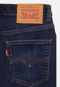 Tmavě modré denimové džíny s oranžovým prošitím, které mají červenou nášivku Levi's na zadní kapse a hnědou koženou nášivku s informacemi o značce.