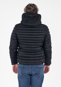 Zwarte donzen jas met horizontale quilt, vaste capuchon en elastische manchetten, gecombineerd met blauwe spijkerbroeken.