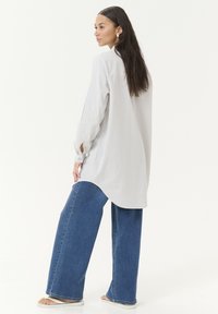 Light gray striped shirt with long sleeves, relaxed fit, and curved hem, paired with wide-leg blue denim jeans. Simple and casual design.
