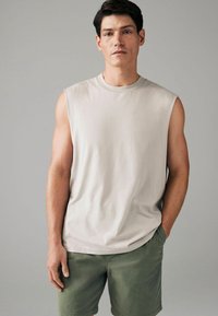 Beige mouwloze T-shirt gemaakt van zachte stof, met een ronde halslijn. Gecombineerd met olijfgroene shorts met een elastische tailleband.