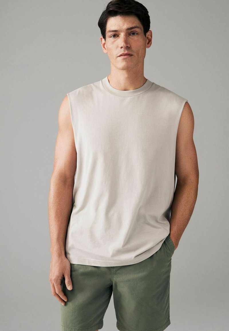 Beige mouwloze T-shirt gemaakt van zachte stof, met een ronde halslijn. Gecombineerd met olijfgroene shorts met een elastische tailleband.