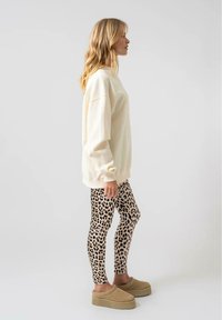 Sudadera oversized de color beige claro con puños acanalados, combinada con leggins ajustados de estampado de leopardo y zapatillas de plataforma beige, vista de lado.