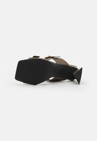 Sandalo alto con tacco triangolare nero, in pelle marrone texturizzata, dotato di due cinturini regolabili e una suola in gomma liscia.