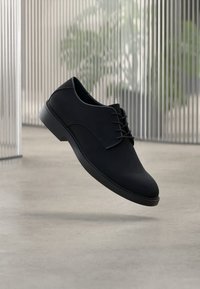 Μαύρο δετό παπούτσι με απαλό, ματ υφή και στρογγυλεμένη μύτη. Μινιμαλιστικός σχεδιασμός με χαμηλό τακούνι και διακριτικές ραφές.