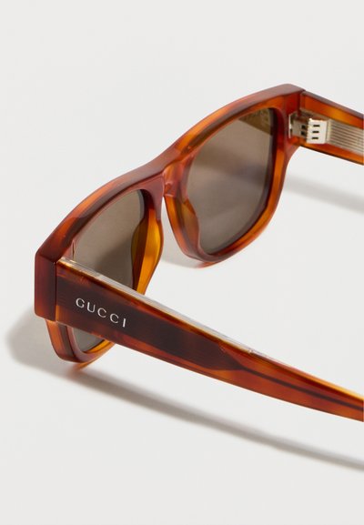 Lunettes de soleil Gucci style écaille avec verres foncés et détails argentés sur la charnière, présentées en gros plan sous un angle.