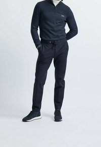 Sudadera de cuello con cremallera en color marino con paneles texturizados en los hombros, combinada con pantalones chinos oscuros con cordón ajustable y zapatillas elegantes.