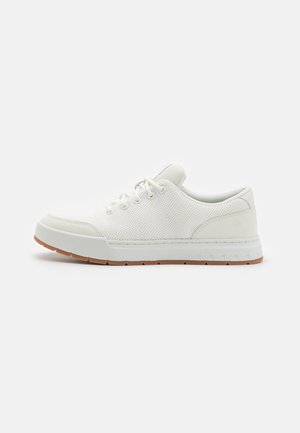 Hvite sneakers med mesh-overdel, rund tå og gummisål med et strukturelt mønster. Har flate snørebånd og diskret merkevare på hælen.