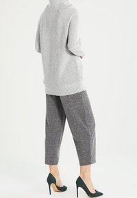 Grå, ribbad tröja med hög krage, kombinerad med korta grå byxor och gröna högklackade skor. Mjuk textur och avslappnad passform.