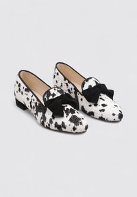 Mocasines de piel de vaca con un patrón a lunares en blanco y negro, acento de lazo negro y un tacón bajo. Textura suave con un diseño de punta afilada.