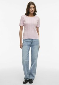 Maglietta rosa a maniche corte con strisce verticali testurizzate, abbinata a jeans a gamba larga blu chiaro e scarpe nere. Outfit semplice e moderno.
