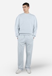Lyseblå bomulds sweatskjorte og matchende sweatpants. Sweatskjorten har en rund hals og ribbede manchetter. Bukserne har en elastisk talje.