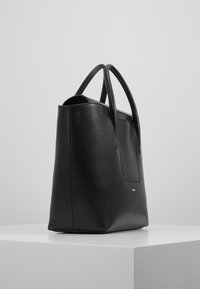 Svart läder tote-väska med strukturerad form, slät yta och sidoficka. Har dubbla handtag och en subtil detaljer i guldlogga.