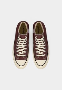 Ζευγάρι μπορντό υψηλά αθλητικά παπούτσια Converse Chuck Taylor με λευκά κορδόνια και καουτσούκ καλύμματα στα δάχτυλα, φωτογραφημένα από πάνω σε λευκό φόντο.