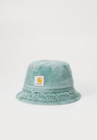 Mintgrøn samt buksedragt hat med bred skygge og et firkantet Carhartt mærke med et gult logo. Teksturflade med lodrette ribber.
