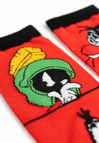 Calzini rossi con bordi neri presenti personaggi dei cartoni animati: Marvin il Marziano in verde e giallo, e un altro personaggio parzialmente visibile. Texture liscia.