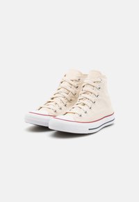 Beige hoge sneakers van canvas, met witte rubberen zolen, zilveren oogjes en gestreepte marineblauwe en rode accenten langs de zool.