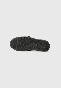 Semelle de chaussure en caoutchouc noir avec un motif de grip texturé, une empreinte de logo et un design nervuré pour une meilleure adhérence.
