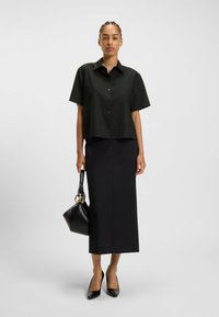 Black short-sleeve button-up shirt with a pocket, paired with a floor-length black skirt, black pointed-toe heels, and a black handbag.