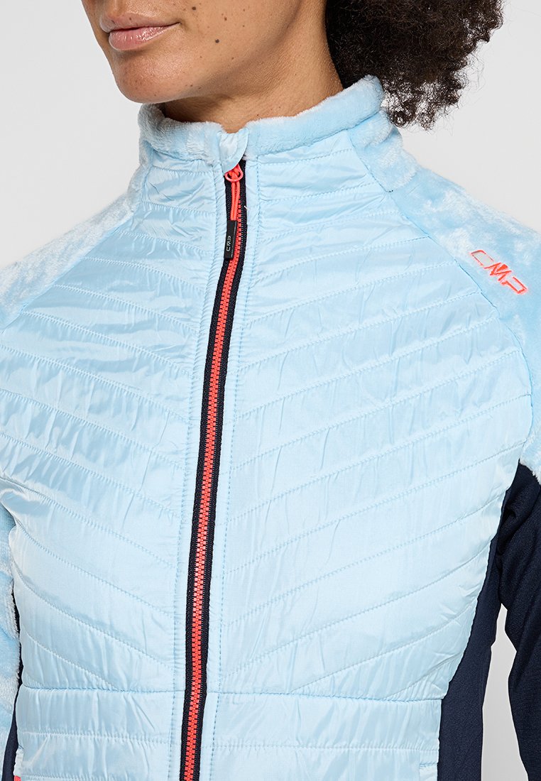 Veste matelassée bleu clair avec un col haut et une fermeture éclair, présentant des manches marines et des accents orange. Texture douce et design ajusté.