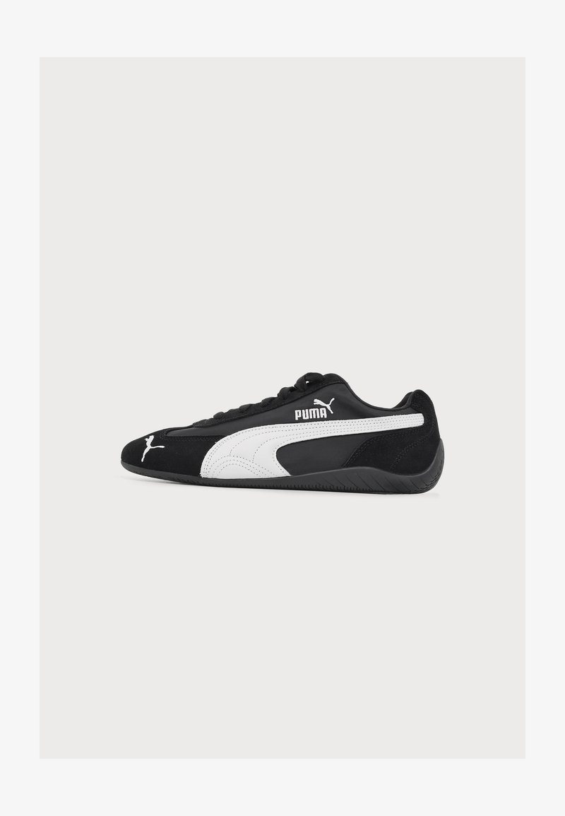 Baskets Puma noires à profil bas avec logo Puma blanc et bande sur le côté, semelle noire et lacets noirs, vues de profil.