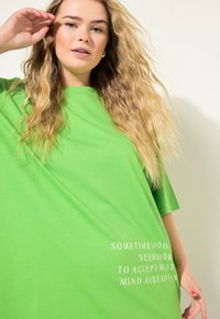Camiseta verde de gran tamaño con mangas cortas, que presenta un texto blanco que dice: "A VECES NECESITAS ACEPTAR LO QUE TU MENTE YA SABE."