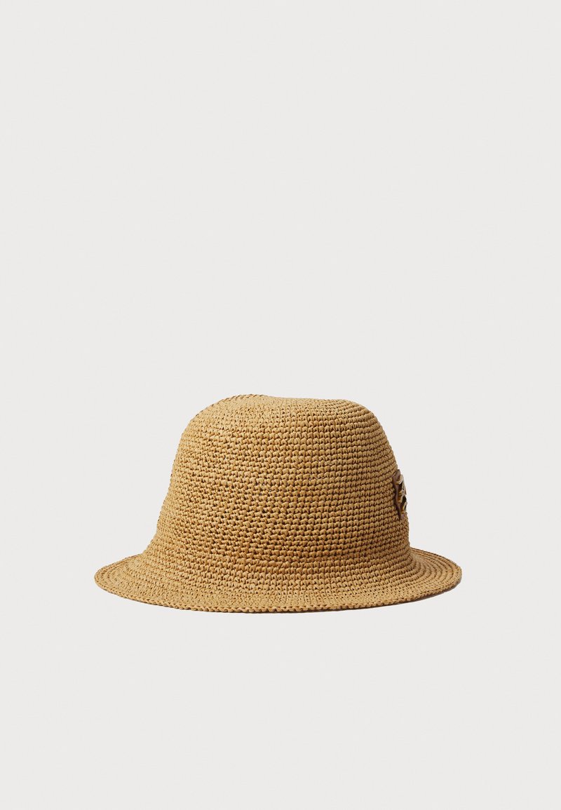 Geflochtener Strohhut in Beige mit einer runden Krone und einem breiten, flexiblen Rand. Verfügt über ein dekoratives Detail an der Seite.