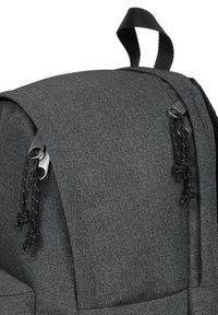 Šedý látkový batoh s texturovaným povrchem, zaobleným vrškem, zipovými zavíráními a černými popruhy pro snadné držení.