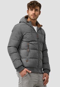 Grå pufferjakke med hette, med en brun fleece-fôret krage, glidelåslommer og ribbestrikkede mansjetter. Glatt tekstur, strukturert design.