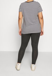 Stribet sort og hvid t-shirt parret med mørkegrå leggings og hvide sneakers, med et simpelt design samt rund hals og korte ærmer.
