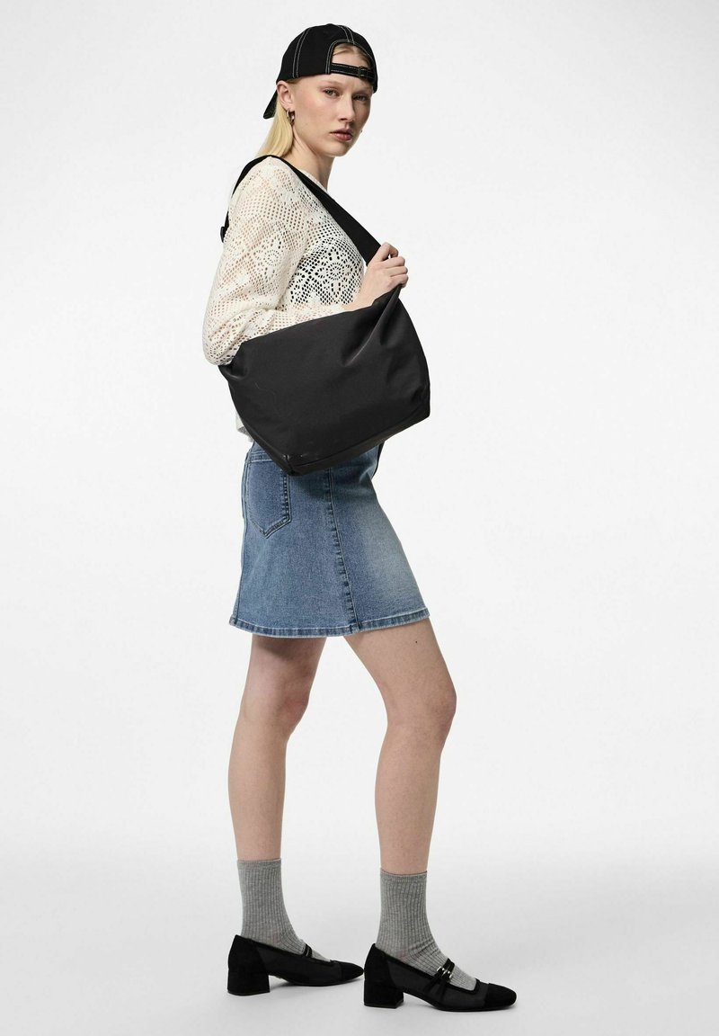 Juodas, minkštas audinys pečių krepšys su plačiu dirželiu. Modelis vilki raštuotą megztinį, džinsinę sijoną, pilkas kojines ir juodas batus.