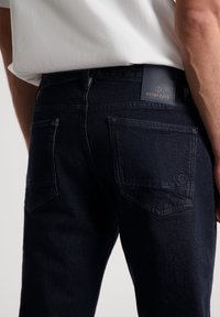 Pantalones de mezclilla azul oscuro con un corte slim, que cuentan con dos bolsillos traseros y una etiqueta de cuero con marca en la cintura. Tejido texturizado.