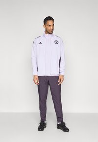 Jasnofioletowa bluza dresowa z czarnym logo i akcentami, w połączeniu z ciemnofioletowymi spodniami. Tkanina wydaje się gładka i sportowa, odpowiednia do uprawiania sportu.