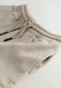 Lys grå svedshorts lavet af blød bomuld, med en elastisk talje med snøre og detaljeret syning langs kanten.