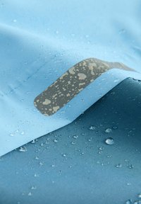 Tessuto resistente all'acqua in azzurro chiaro e blu scuro, con gocce sulla superficie e una patch grigia con un motivo sottile.
