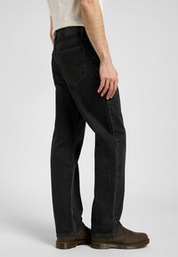 Sorte denim jeans med rett ben-design, som har fem lommer, subtil falming og en teksturert overflate. Brune sko med lav profil.