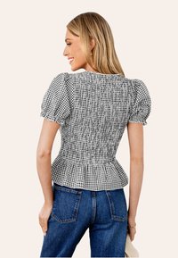 Geplooide zwart-wit ruitjesblouse met korte pofmouwen en een peplum taille, gecombineerd met blauwe spijkerbroeken.