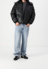 Svart vadderad jacka med huva, med dragkedja och elastiska ärmar. Kombinerad med ljusblå löst sittande jeans och svarta sneakers.