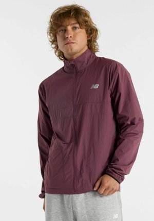 Letvægts, maroon vindjakke med høj krave, lynlåslukning og et New Balance-logo på venstre bryst. Glat tekstur.