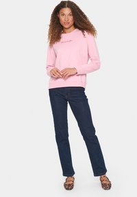 Sudadera rosa clara con texto bordado, cuello redondo y mangas largas, combinada con jeans azul oscuro y zapatos planos de estampado de leopardo.