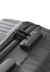 Maleta rígida negra con una superficie texturizada, cremalleras dobles y un candado de combinación; presenta una marca visible y acentos de hardware sólidos.
