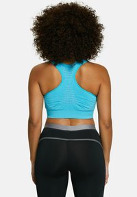 Sujetador deportivo azul claro con diseño de tirantes cruzados en la espalda, material texturizado y detalle fruncido en la parte trasera, combinado con mallas negras de cintura alta.