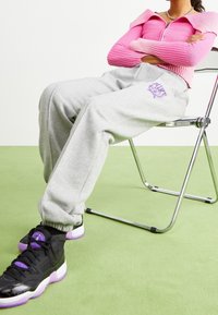 Grå sweatpants med elastiska muddar, prydda med en lila Nike-logga; i kombination med svarta skor med lila detaljer, sittande på en kromstol.