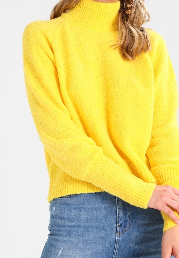 Bright yellow knitted sweater with a high neckline, ribbed cuffs, and a soft, textured finish. Worn with blue denim jeans.